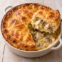 AI illustration of a golden puff pastry chicken pie with a portion removed to show mushrooms, leeks and creamy sauce.
